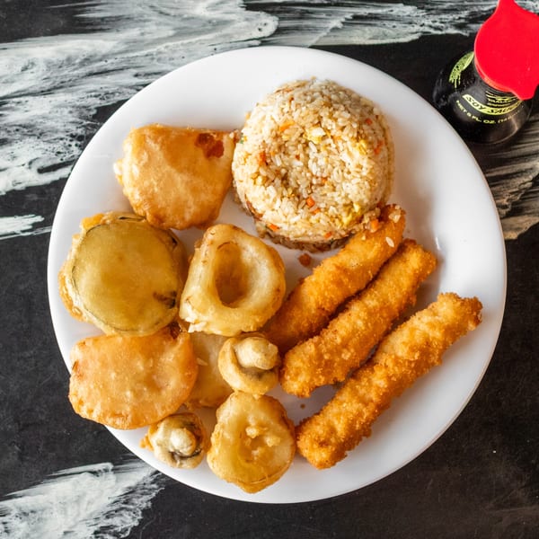 A white plate with fried rice, tempura vegetables, and fried chicken strips, with a soy sauce bottle.