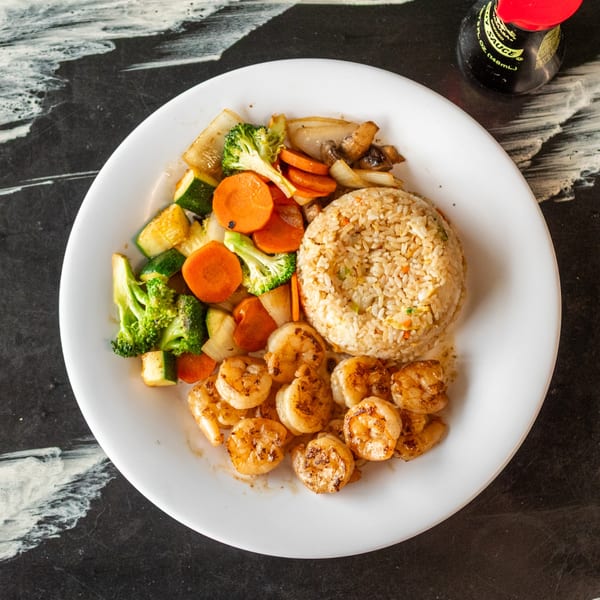 A white plate with grilled shrimp, fried rice, and mixed vegetables on a dark marbled surface.