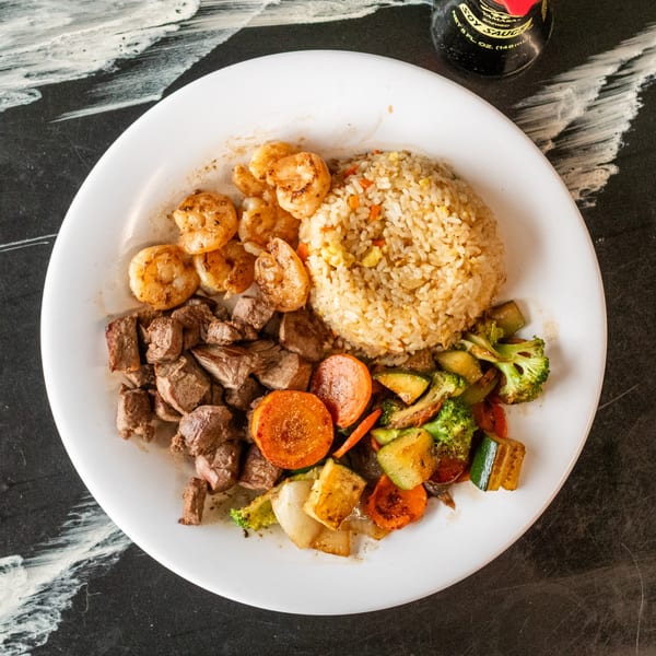 Hibachi plate with shrimp, steak, fried rice, and mixed vegetables on a white plate with soy sauce.
