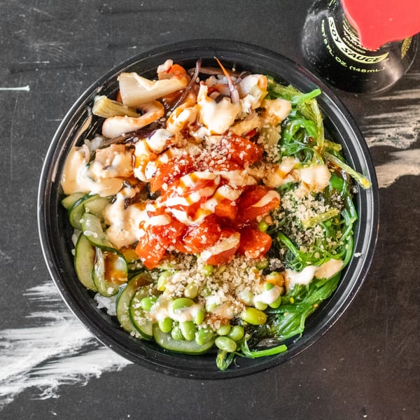 Overhead view of a colorful poke bowl with tuna, seaweed, cucumber, edamame, and sauces.