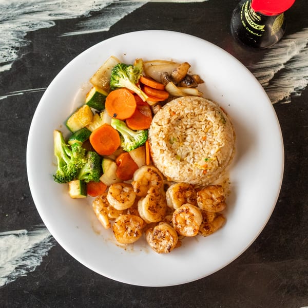 A white plate with shrimp, fried rice, and mixed vegetables, with a soy sauce bottle nearby.