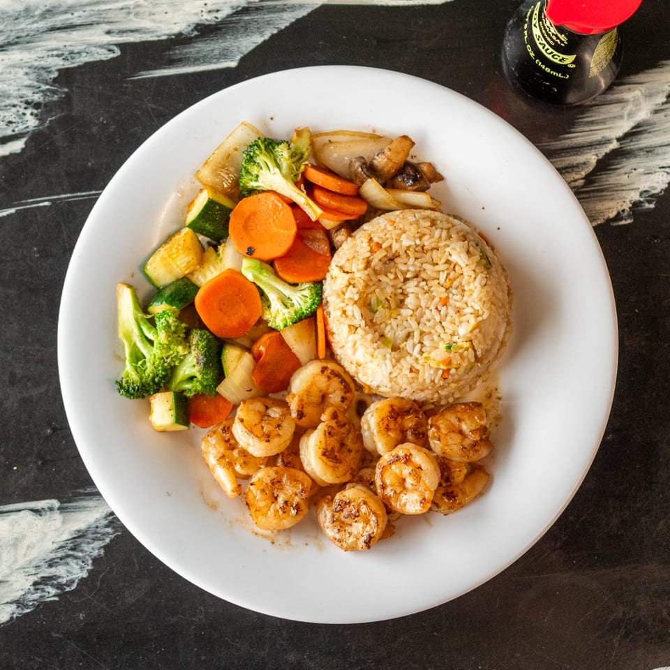 A white plate with shrimp, fried rice, and mixed vegetables, with a soy sauce bottle nearby.