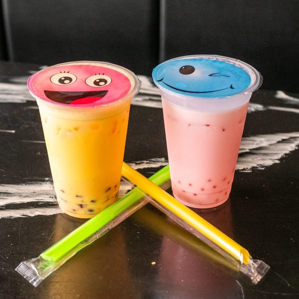 Two colorful bubble tea drinks with smiley face lids and straws on a dark marble surface.