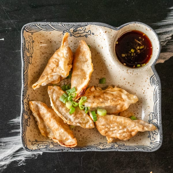 Golden-brown fried dumplings with green onions and a side of soy sauce on a decorative plate.